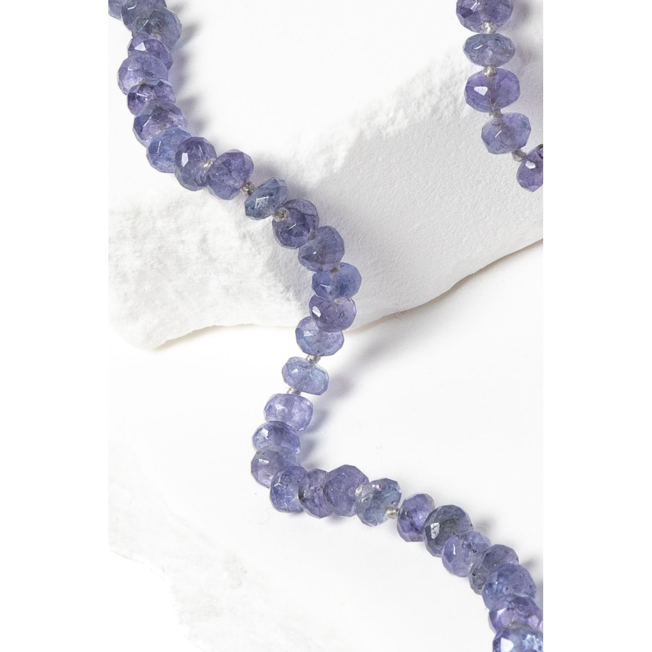 Close-up of faceted tanzanite rondelle gemstones showing luminous blue and lavender tones with subtle gray undertones, individually knotted to enhance movement and durability