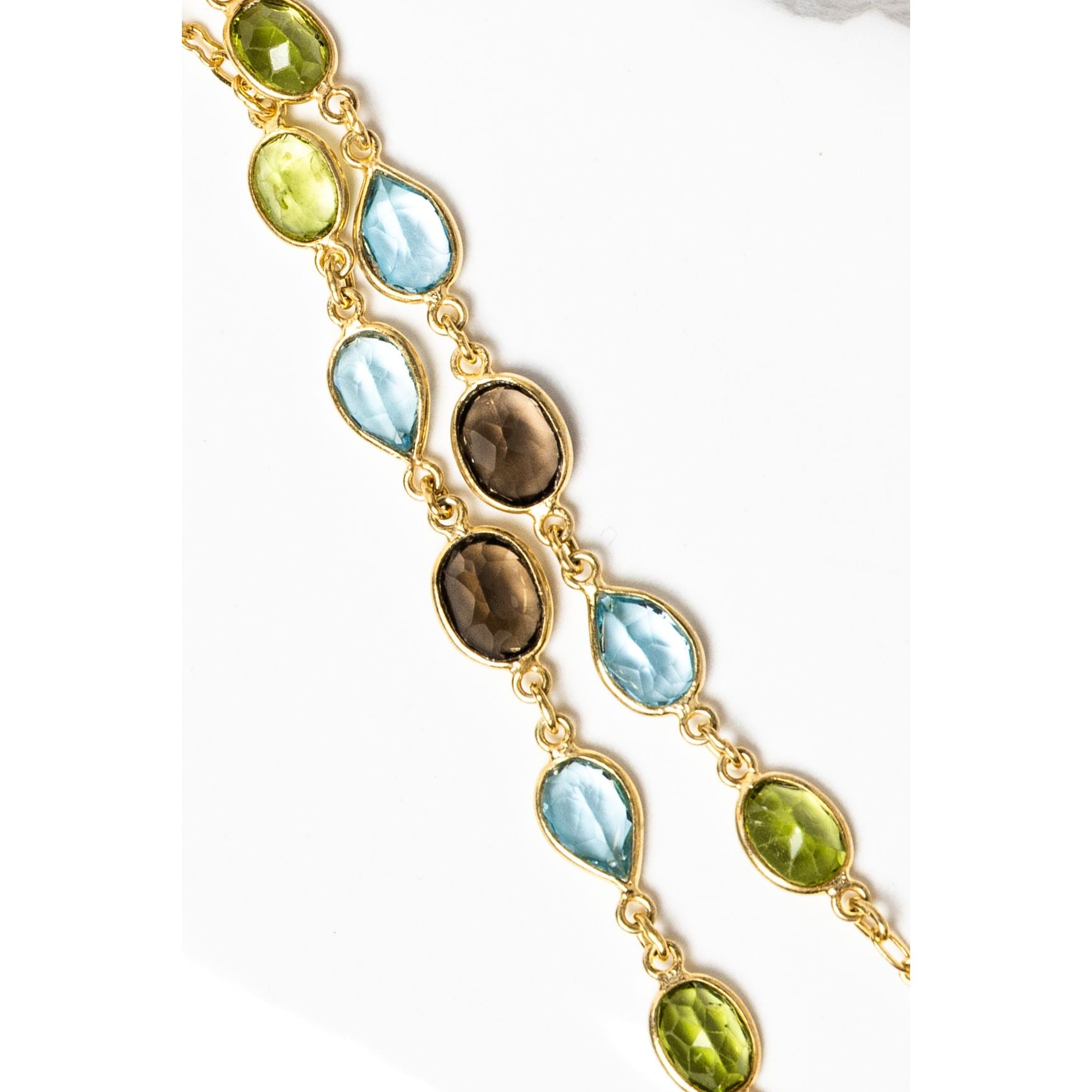 Close-up of the Rare Harmony necklace highlighting smoky quartz, blue topaz, and peridot gemstones in bezel settings along a fine gold chain, revealing the richness of color and refined craftsmanship.