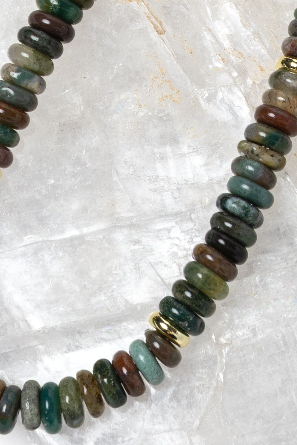 Close-up detail of polished multicolor gemstone rondelles featuring rich green, teal, brown, olive, and smoky natural tones with gold accent spacers.