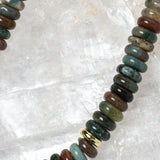 Close-up detail of polished multicolor gemstone rondelles featuring rich green, teal, brown, olive, and smoky natural tones with gold accent spacers.