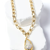 Luxury necklace featuring a luminous natural baroque pearl pendant suspended from a sculptural gold-plated circular-link chain with polished metallic accents and an artistic contemporary silhouette.