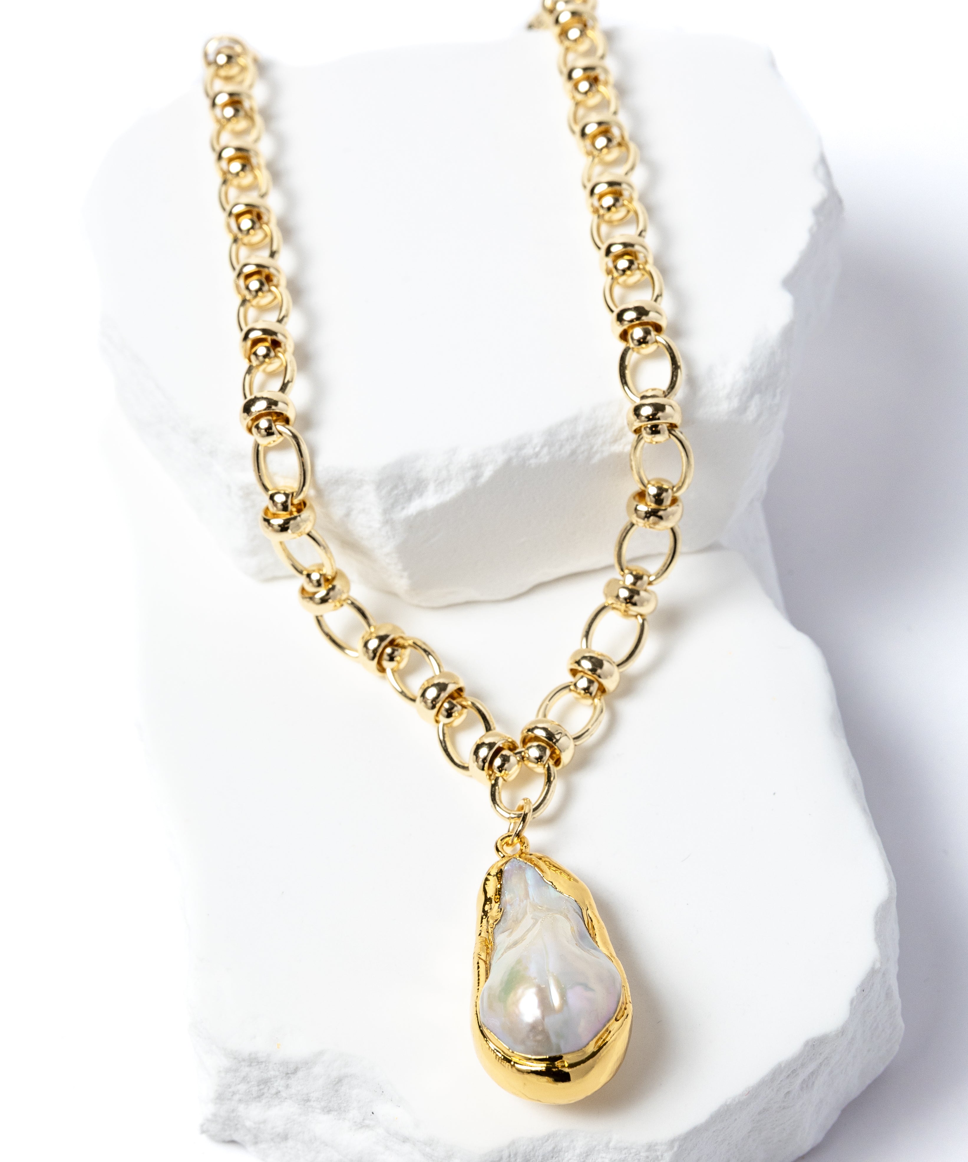 Luxury necklace featuring a luminous natural baroque pearl pendant suspended from a sculptural gold-plated circular-link chain with polished metallic accents and an artistic contemporary silhouette.
