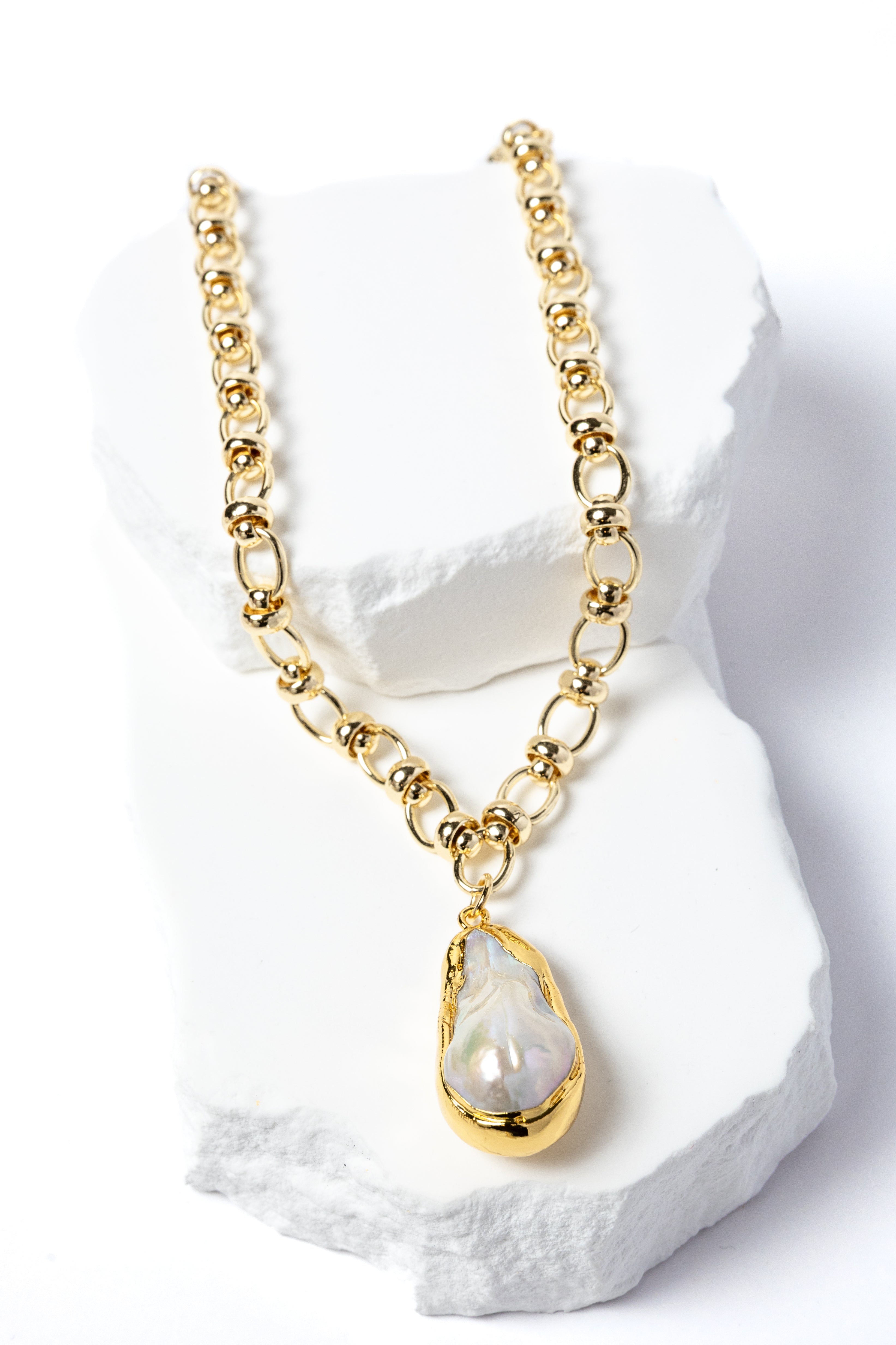 Luxury necklace featuring a luminous natural baroque pearl pendant suspended from a sculptural gold-plated circular-link chain with polished metallic accents and an artistic contemporary silhouette.
