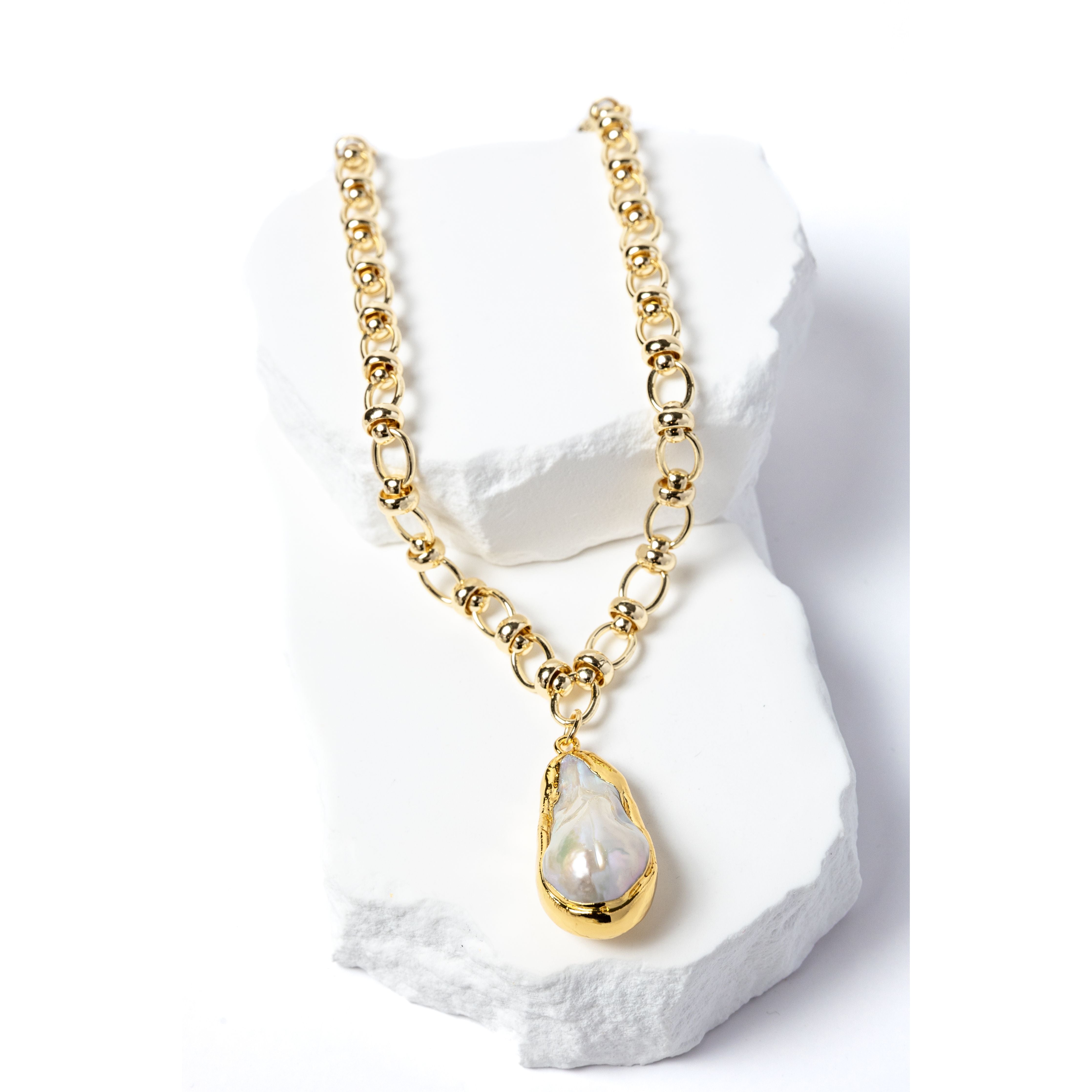 Luxury necklace featuring a luminous natural baroque pearl pendant suspended from a sculptural gold-plated circular-link chain with polished metallic accents and an artistic contemporary silhouette.