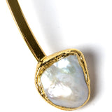 Close-up detail of a luminous natural baroque pearl suspended from a polished gold-plated sculptural setting with organic contours and refined handcrafted detailing.
