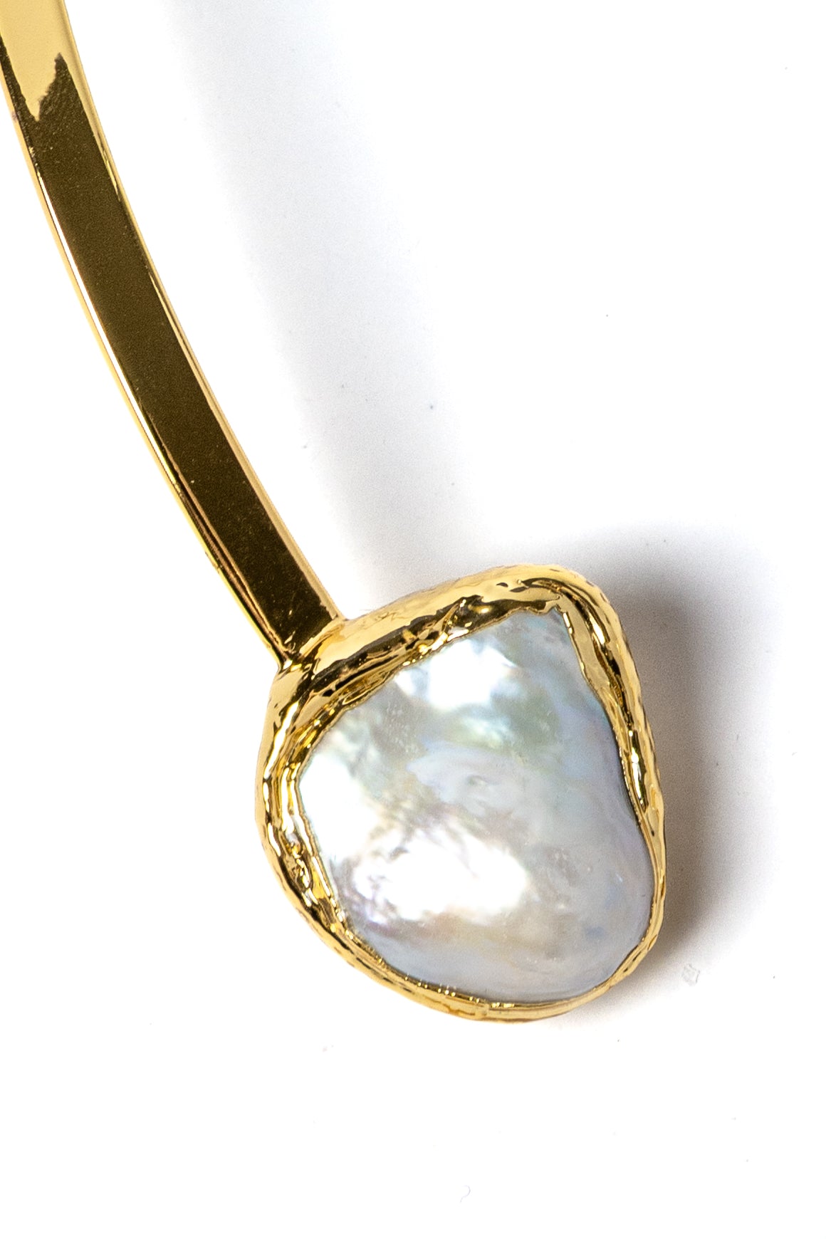 Close-up detail of a luminous natural baroque pearl suspended from a polished gold-plated sculptural setting with organic contours and refined handcrafted detailing.
