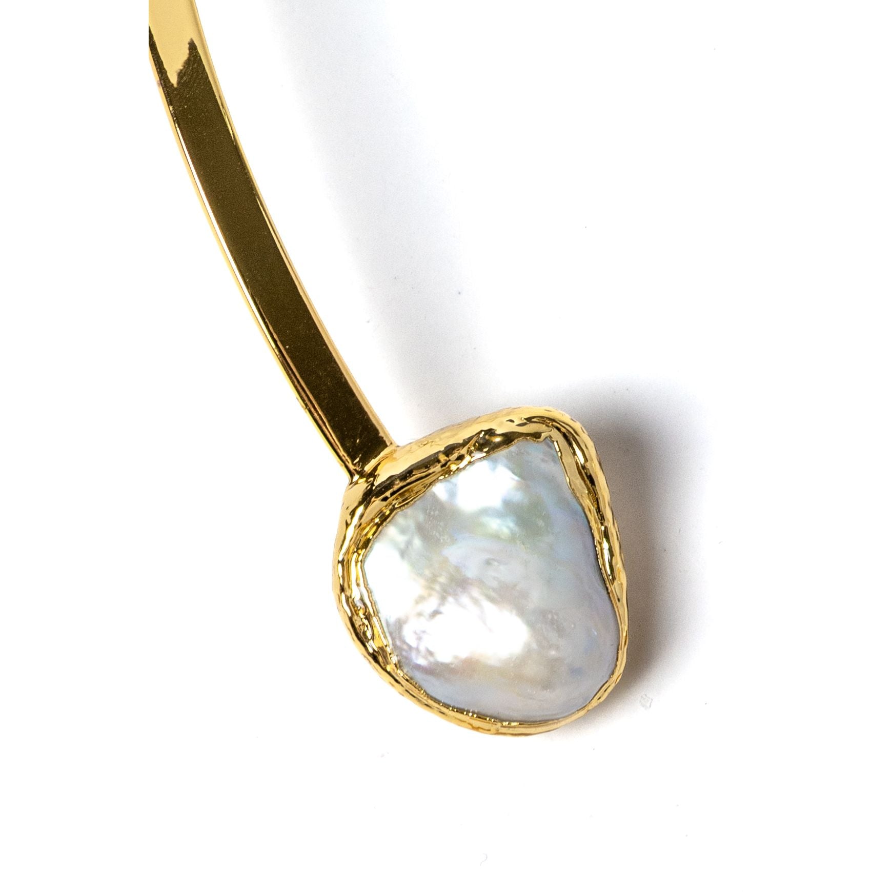 Close-up detail of a luminous natural baroque pearl suspended from a polished gold-plated sculptural setting with organic contours and refined handcrafted detailing.