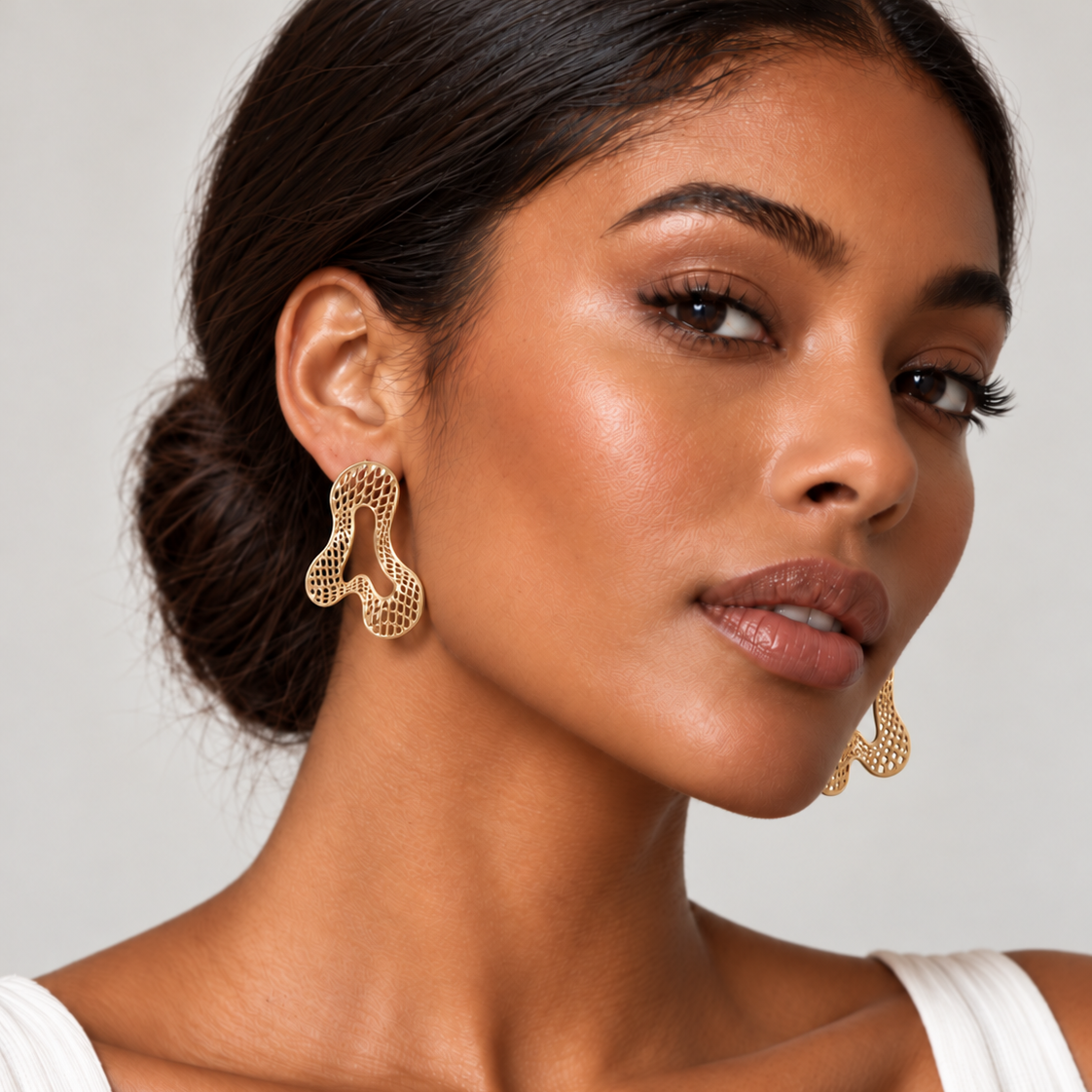 Model wearing sculptural gold-tone statement earrings featuring an organic, flowing silhouette with intricate openwork mesh detailing and delicate cutouts. Approximately 1.6 inches long.