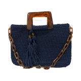 Hand-crocheted Monique handbag in deep navy blue with a warm marbled resin top handle, coordinating resin chain strap, and double tassel detail.