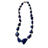 One-of-a-kind lapis stone necklace featuring organically shaped cobalt-blue gemstones separated by gold-plated spacers in a sculptural statement design.