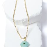 Natural Amazonite Gem Charm Necklace featuring a faceted soft aqua gemstone pendant with a green cubic zirconia accent suspended from a gold-plated beaded chain displayed on a white sculptural stone backdrop.