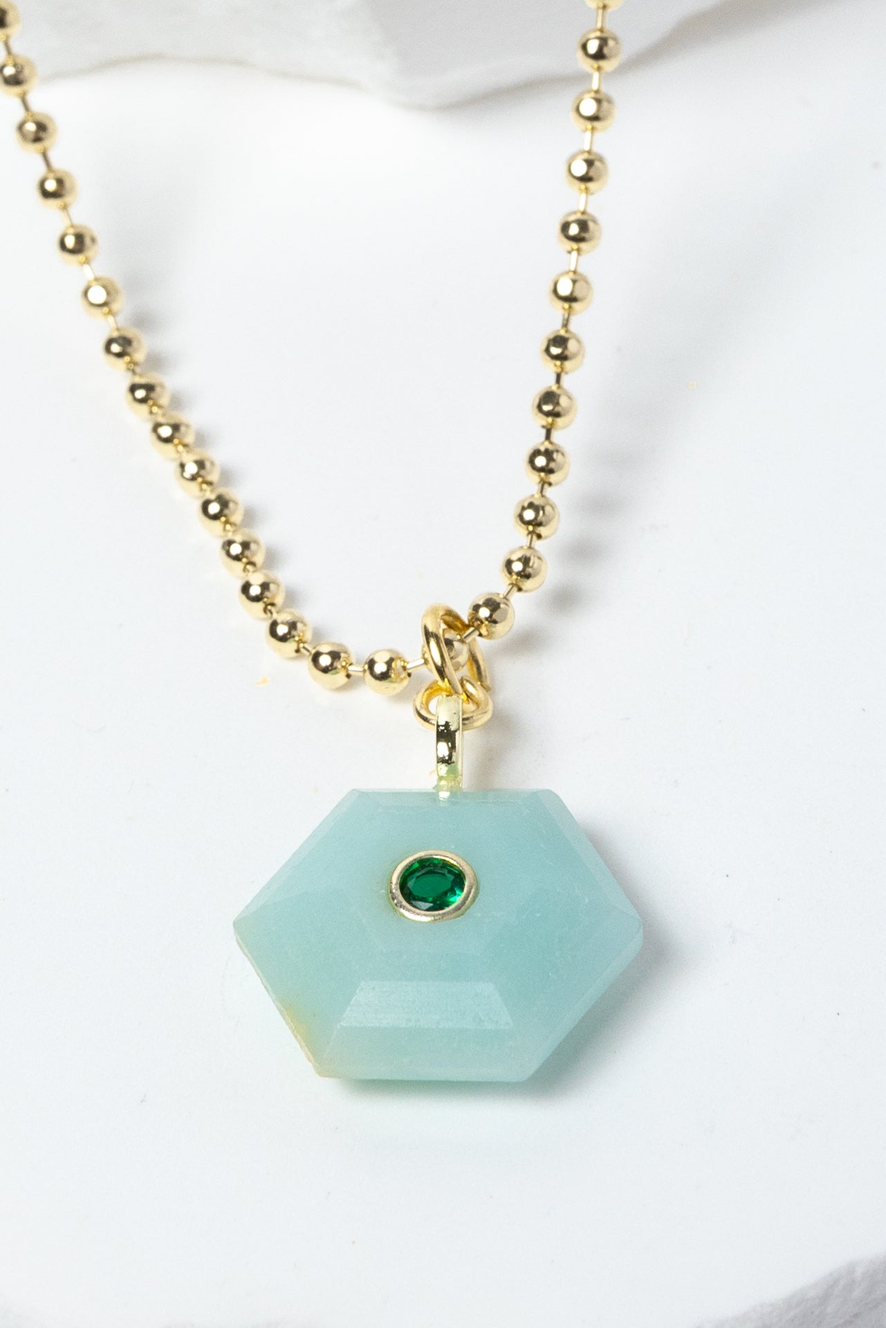 Close-up of a natural Amazonite pendant showcasing serene aqua-blue tones, faceted geometric shape, green cubic zirconia detail, and gold-plated setting.