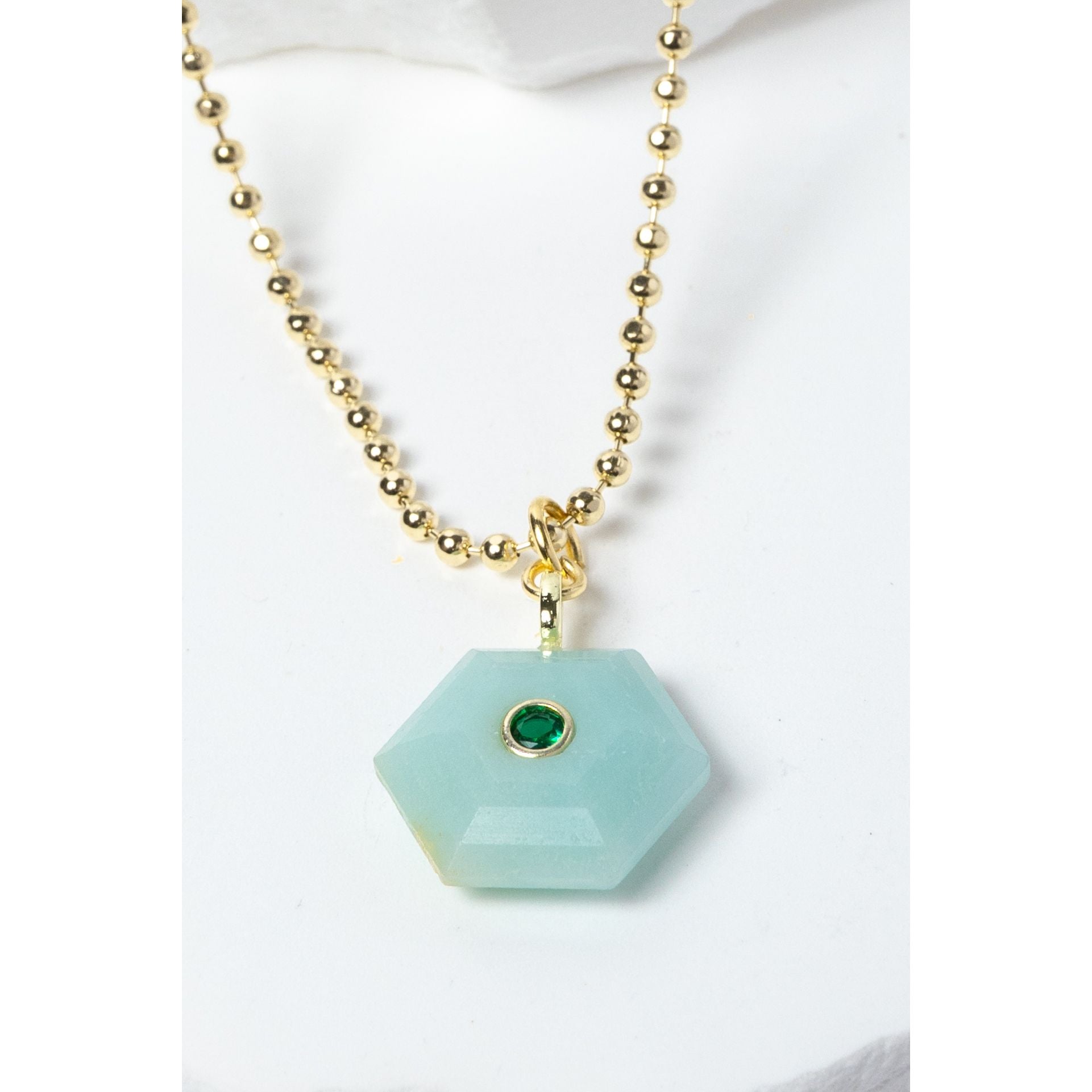 Close-up of a natural Amazonite pendant showcasing serene aqua-blue tones, faceted geometric shape, green cubic zirconia detail, and gold-plated setting.