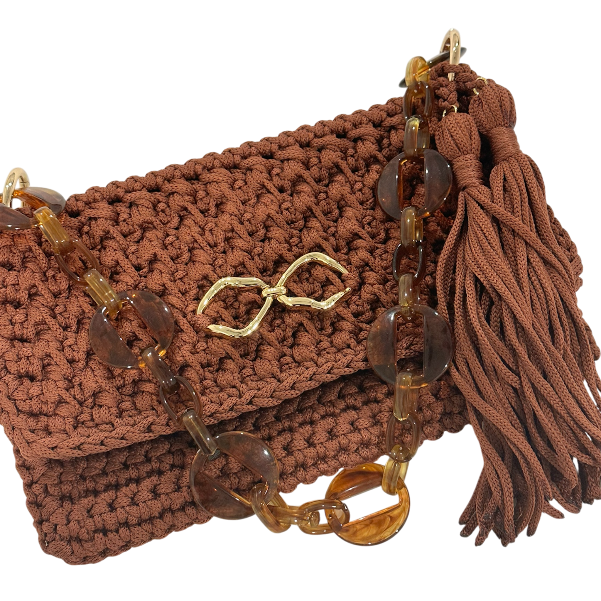 Close-up of the Polly Clutch in a rich cinnamon-brown tone featuring dimensional handcrafted crochet texture, translucent amber-inspired resin chain strap, polished gold-tone front accent, and elongated tassel detail with sculptural movement.