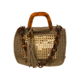 Caramel handcrafted luxury handbag with architectural woven rattan center, dimensional crochet frame, marbled resin handles, sculptural chain strap, and tassel detail. The unlined open silhouette includes a discreet transparent insert pocket and a refined compact structure displayed against a neutral background.