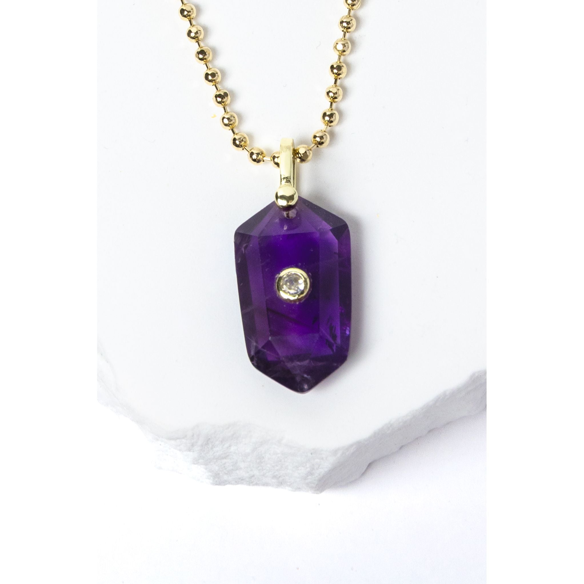 Close-up of a natural Amethyst pendant showcasing rich violet-purple tones, faceted geometric shape, cubic zirconia detail, and gold-plated setting.