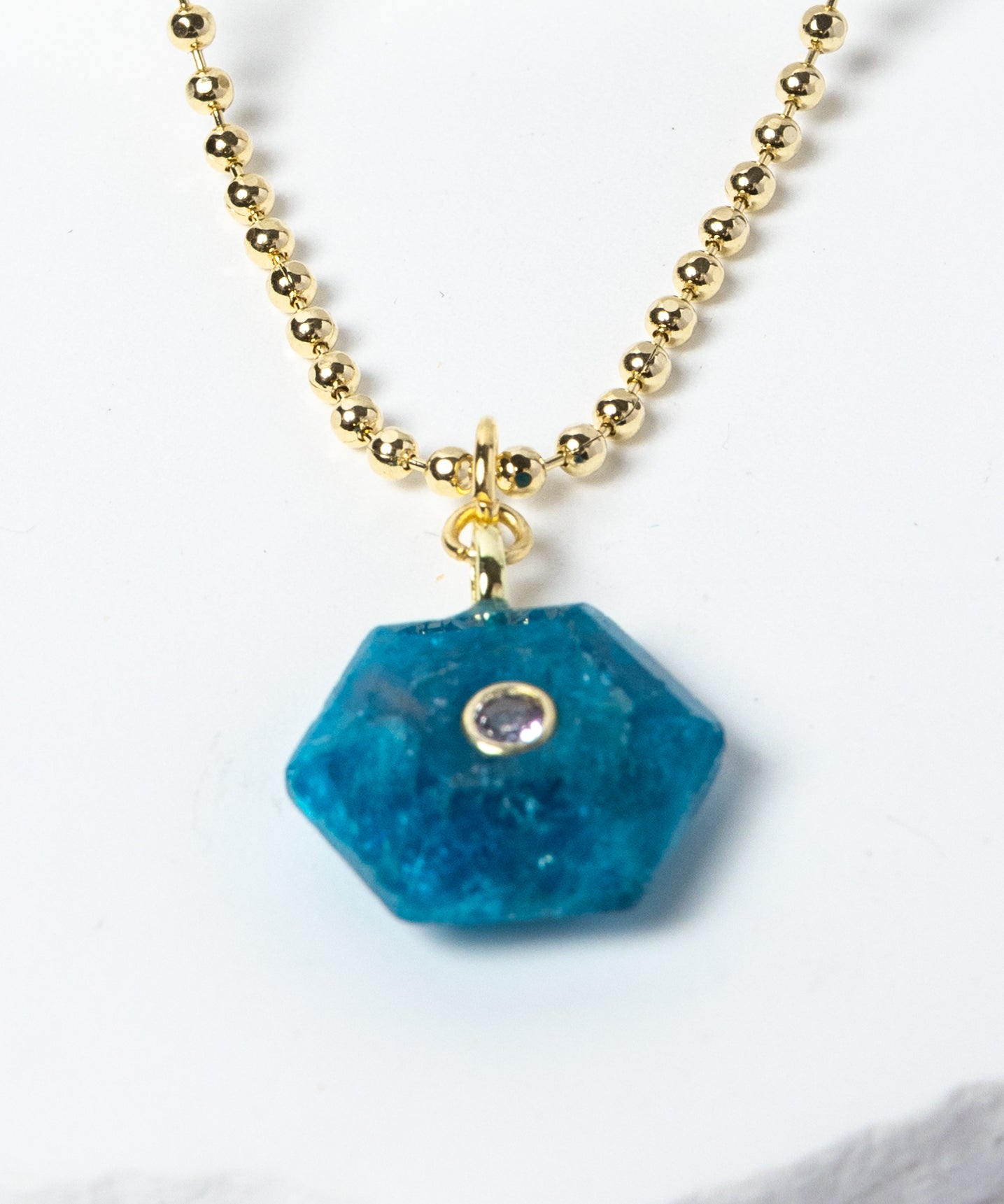 Close-up of a natural Apatite gemstone pendant showcasing vivid ocean-blue tones, faceted geometric shape, cubic zirconia detail, and gold-plated setting.