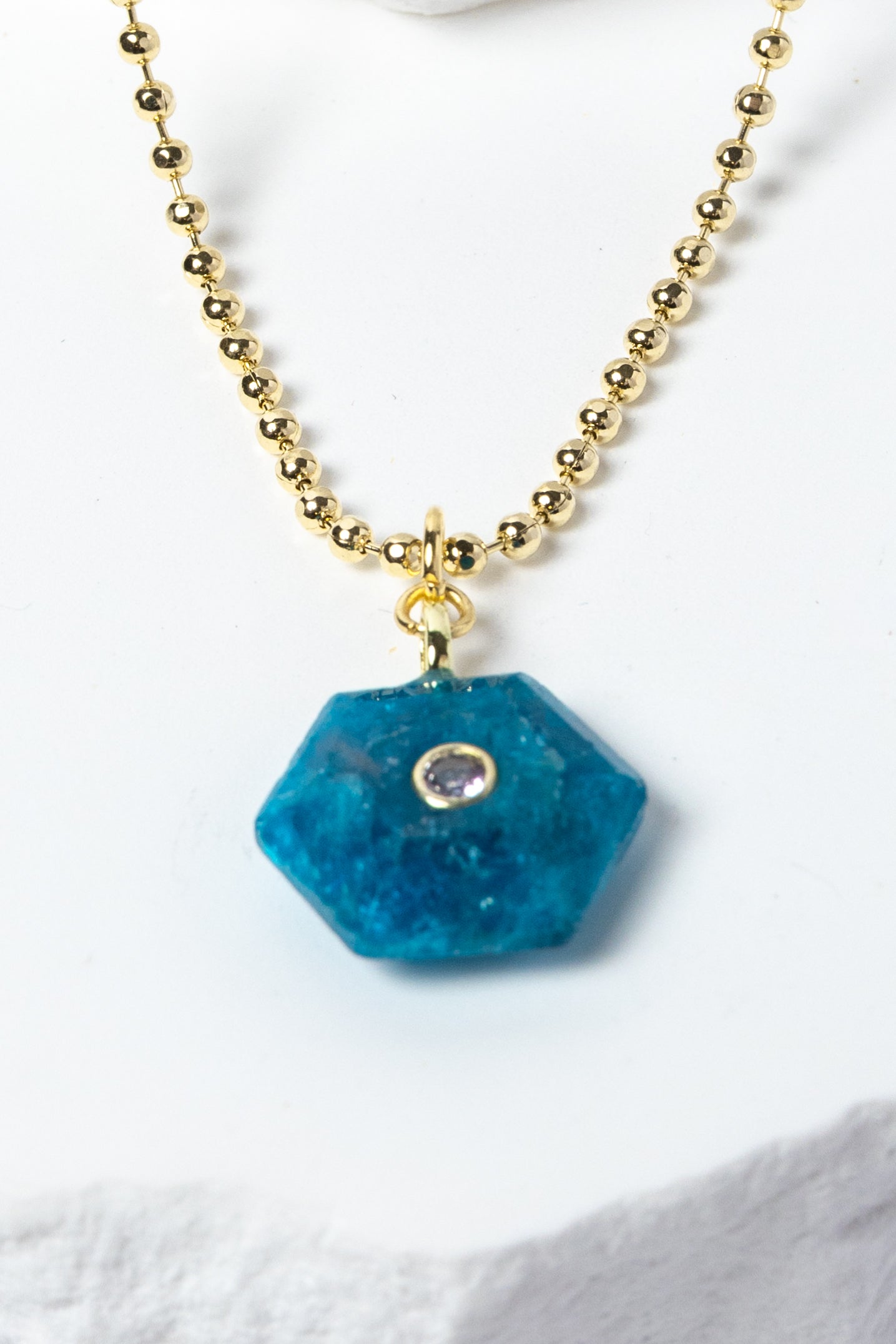 Close-up of a natural Apatite gemstone pendant showcasing vivid ocean-blue tones, faceted geometric shape, cubic zirconia detail, and gold-plated setting.