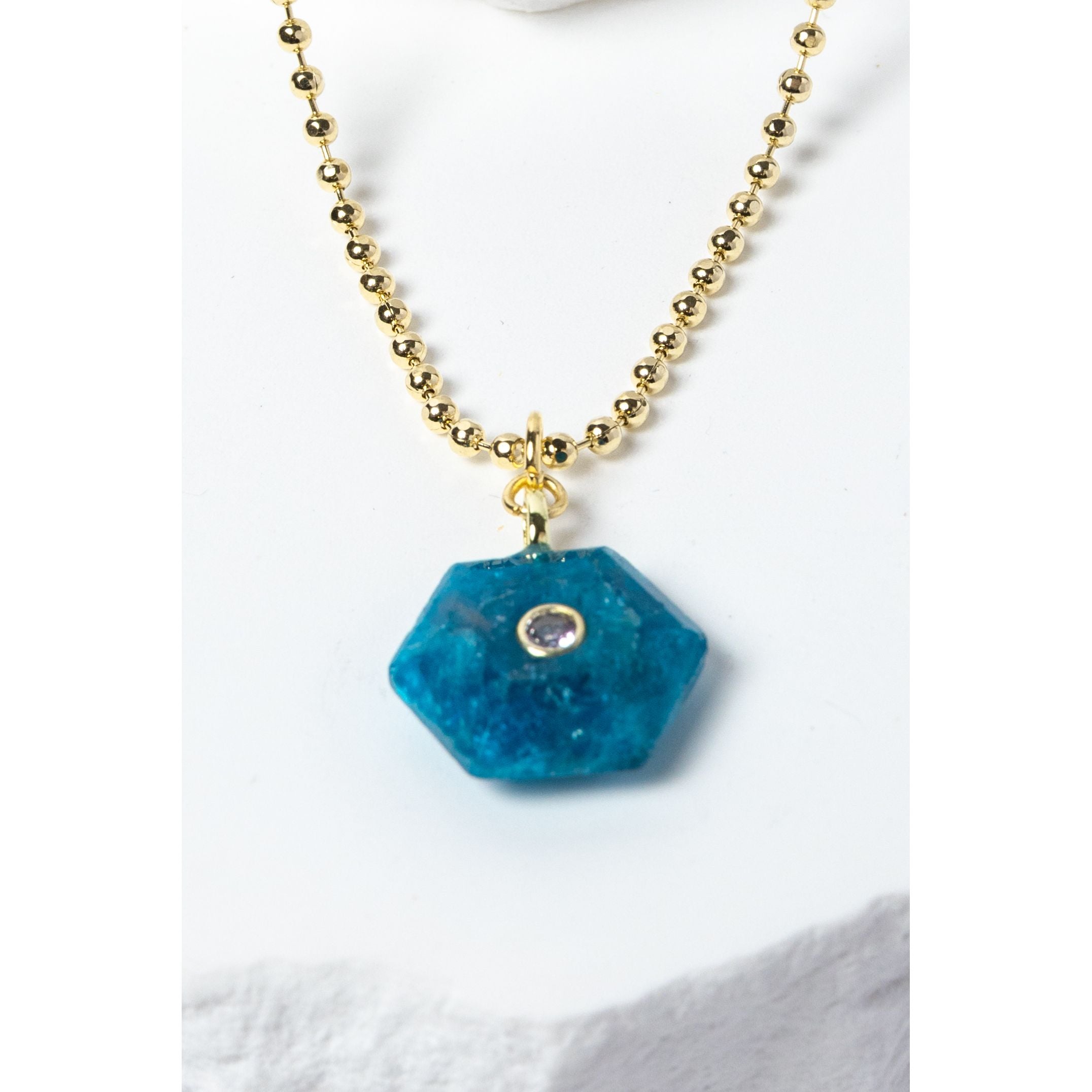 Close-up of a natural Apatite gemstone pendant showcasing vivid ocean-blue tones, faceted geometric shape, cubic zirconia detail, and gold-plated setting.