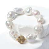 Baroque pearl bracelet featuring luminous freshwater pearls and a pavé-set gold clasp displayed on a sculptural white stone backdrop.