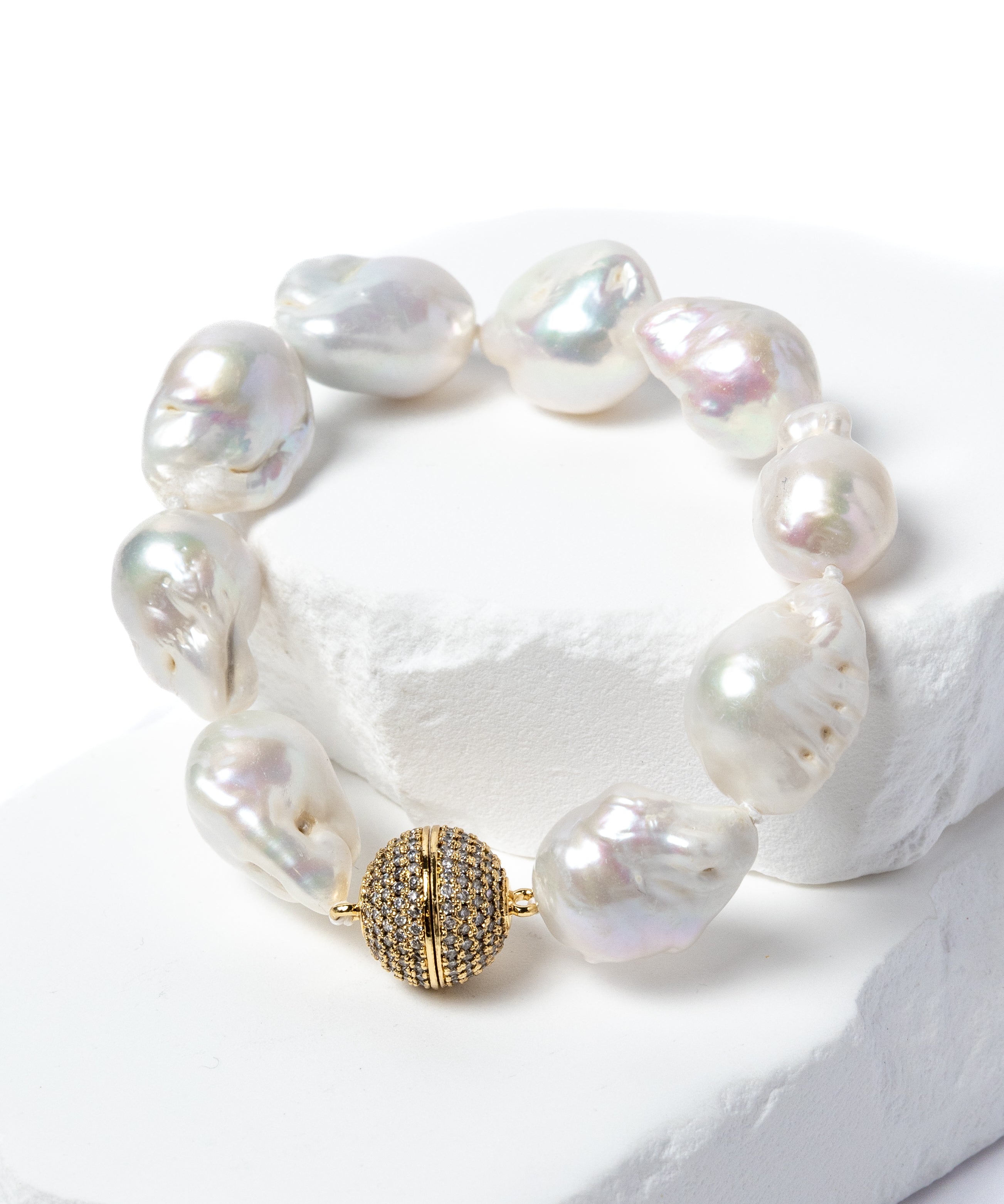Baroque pearl bracelet featuring luminous freshwater pearls and a pavé-set gold clasp displayed on a sculptural white stone backdrop.