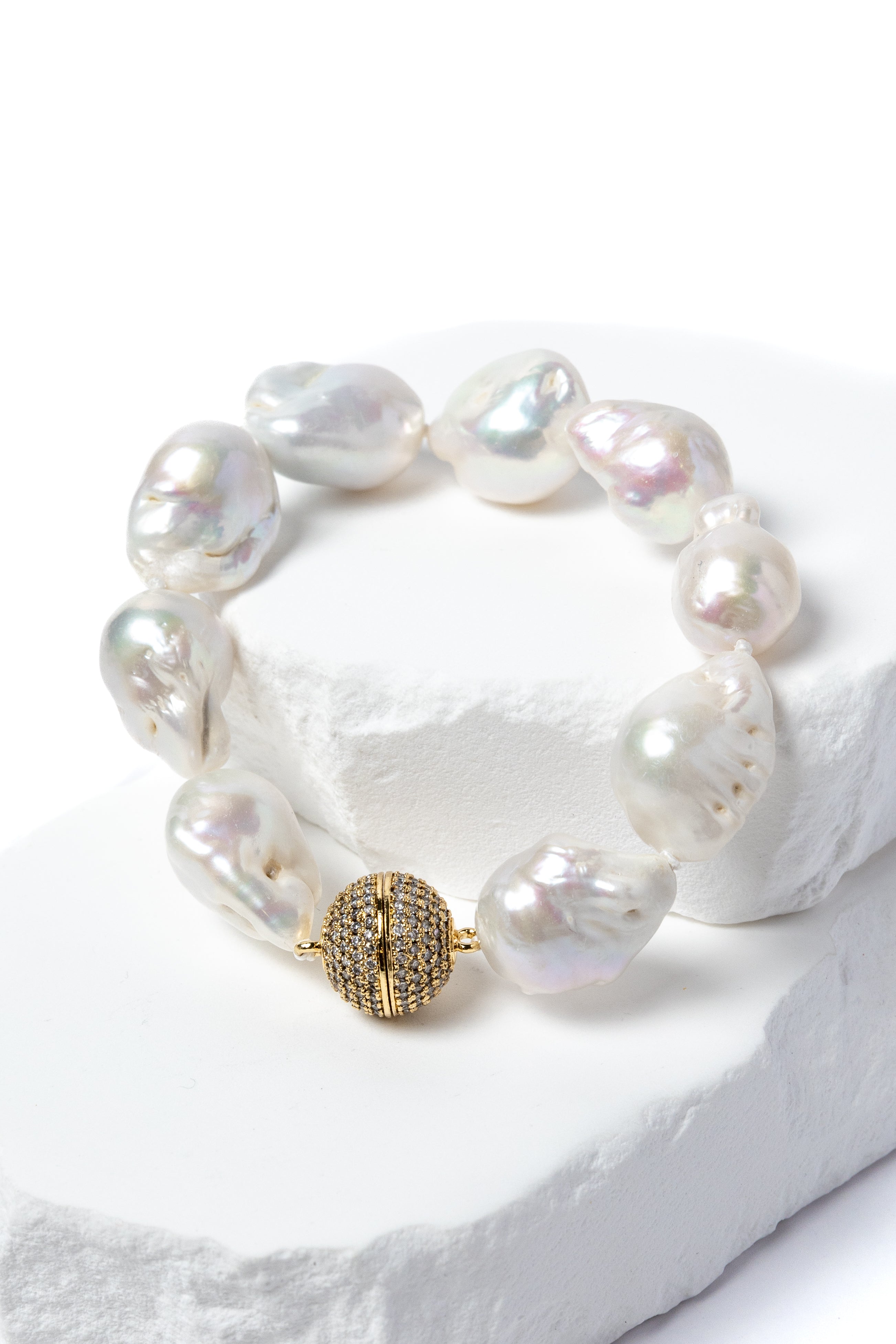 Baroque pearl bracelet featuring luminous freshwater pearls and a pavé-set gold clasp displayed on a sculptural white stone backdrop.