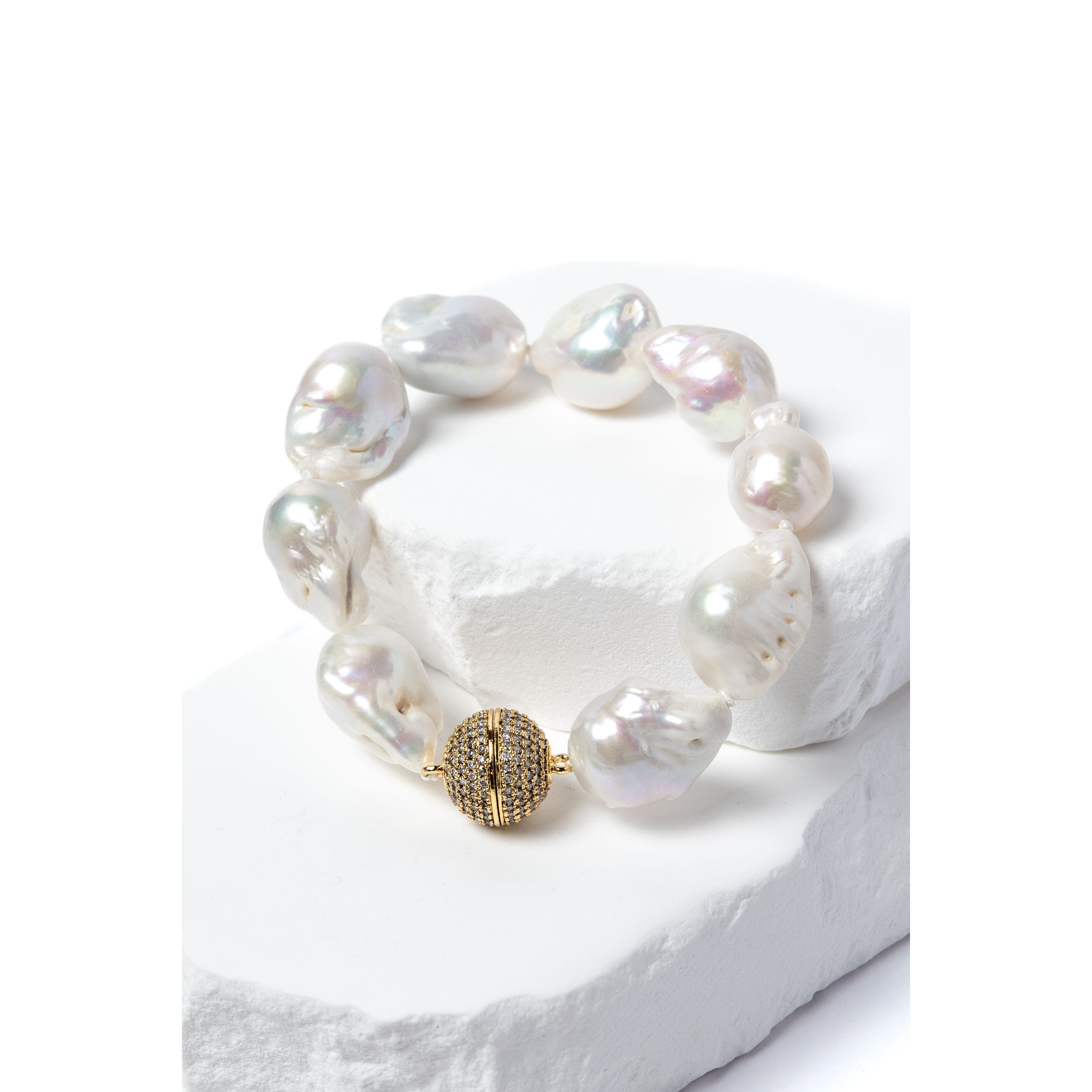 Baroque pearl bracelet featuring luminous freshwater pearls and a pavé-set gold clasp displayed on a sculptural white stone backdrop.