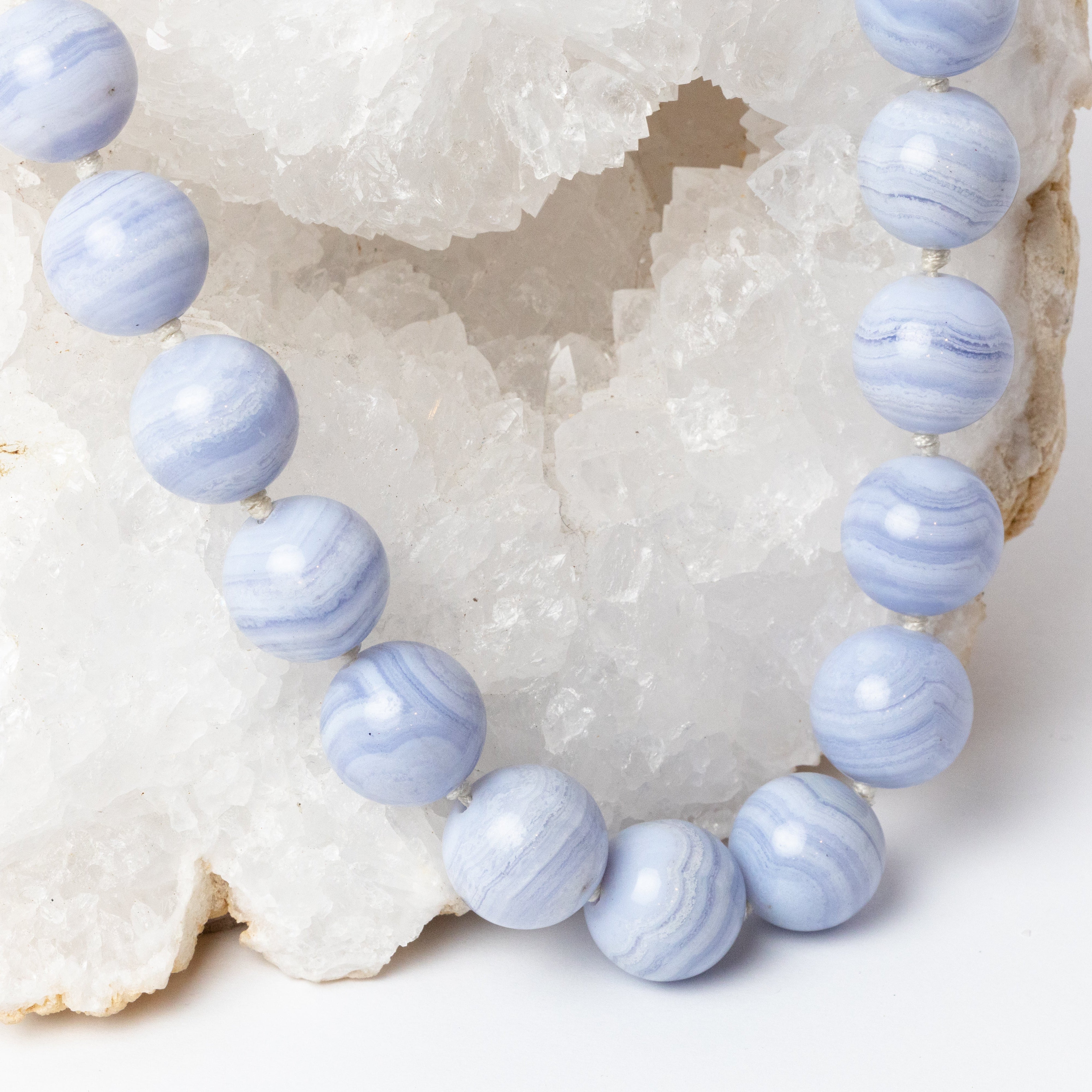 Close-up of round blue lace agate stones showing delicate blue, white, and lavender banding and individual knots between the beads.