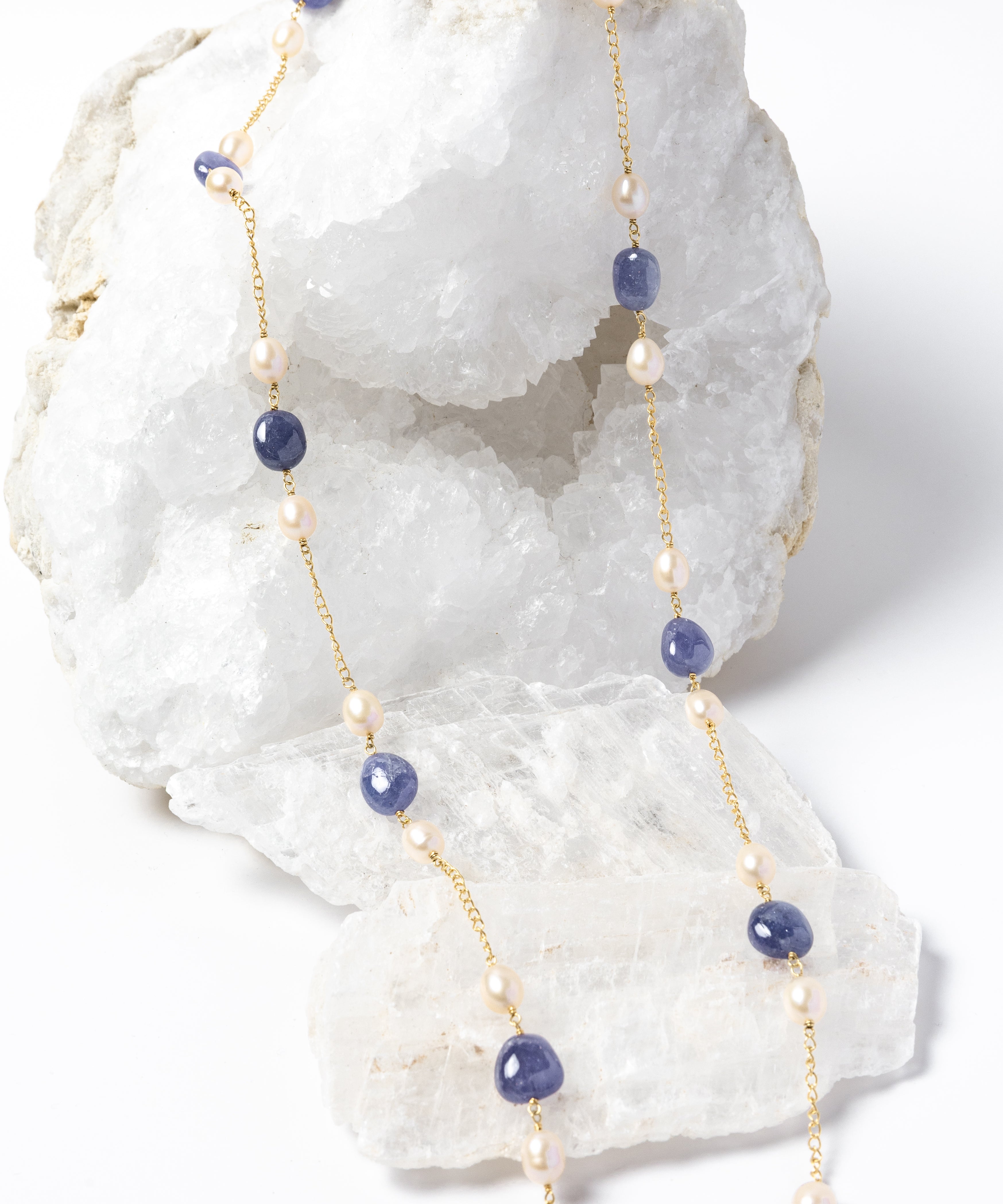 Blue Waltz long necklace featuring natural tanzanite gemstones and freshwater pearls arranged along a gold-plated chain with an elegant fluid silhouette.