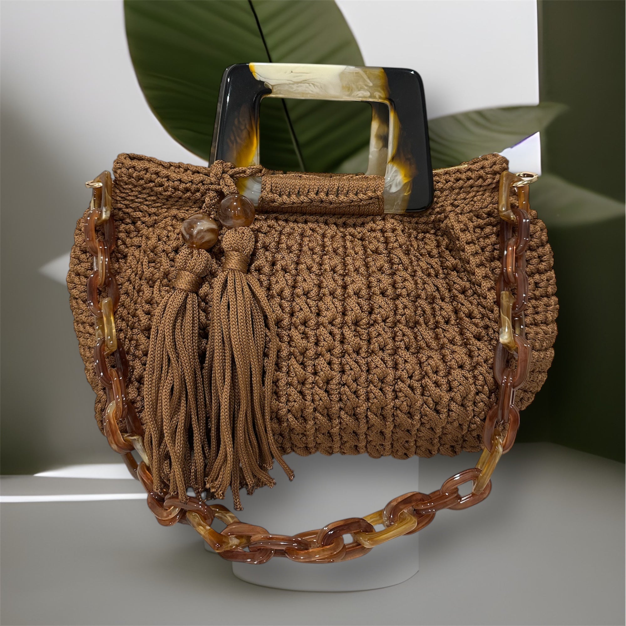 
Hand-crocheted Giselle handbag in a warm cognac tone with dimensional vertical textured stitching, featuring marbled amber resin round handles and a coordinating chain strap.
