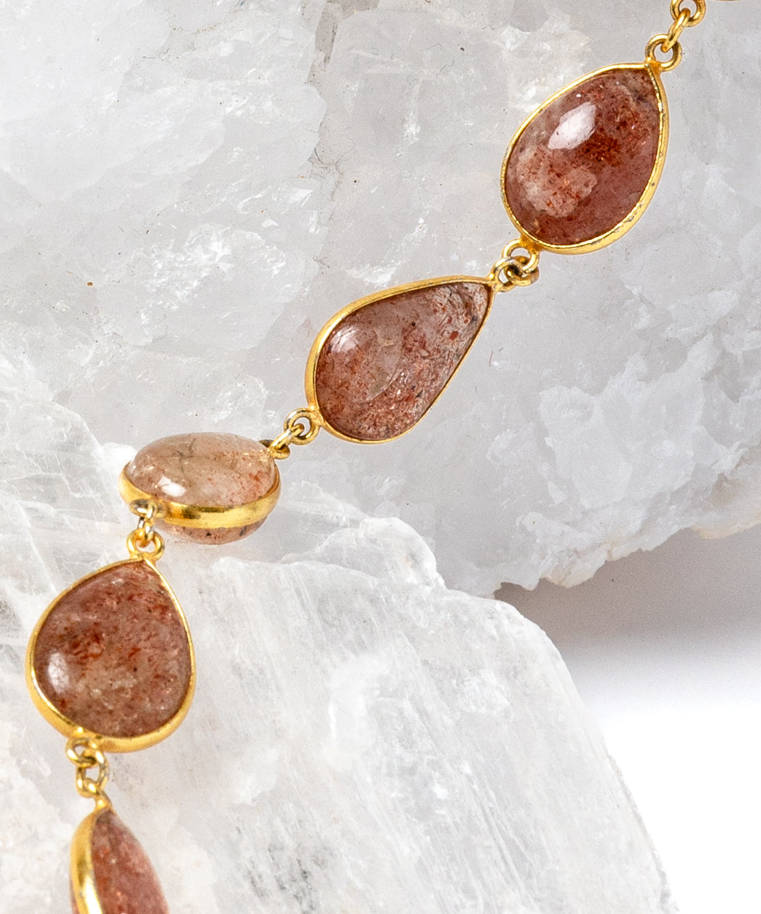     Close-up of natural sunstone gemstones in warm copper, peach, and amber tones with gold-plated settings.