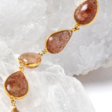     Close-up of natural sunstone gemstones in warm copper, peach, and amber tones with gold-plated settings.