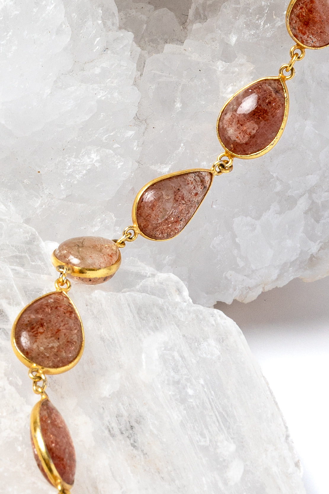     Close-up of natural sunstone gemstones in warm copper, peach, and amber tones with gold-plated settings.