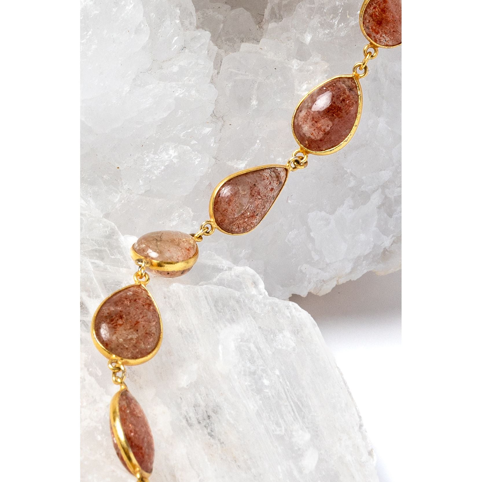     Close-up of natural sunstone gemstones in warm copper, peach, and amber tones with gold-plated settings.