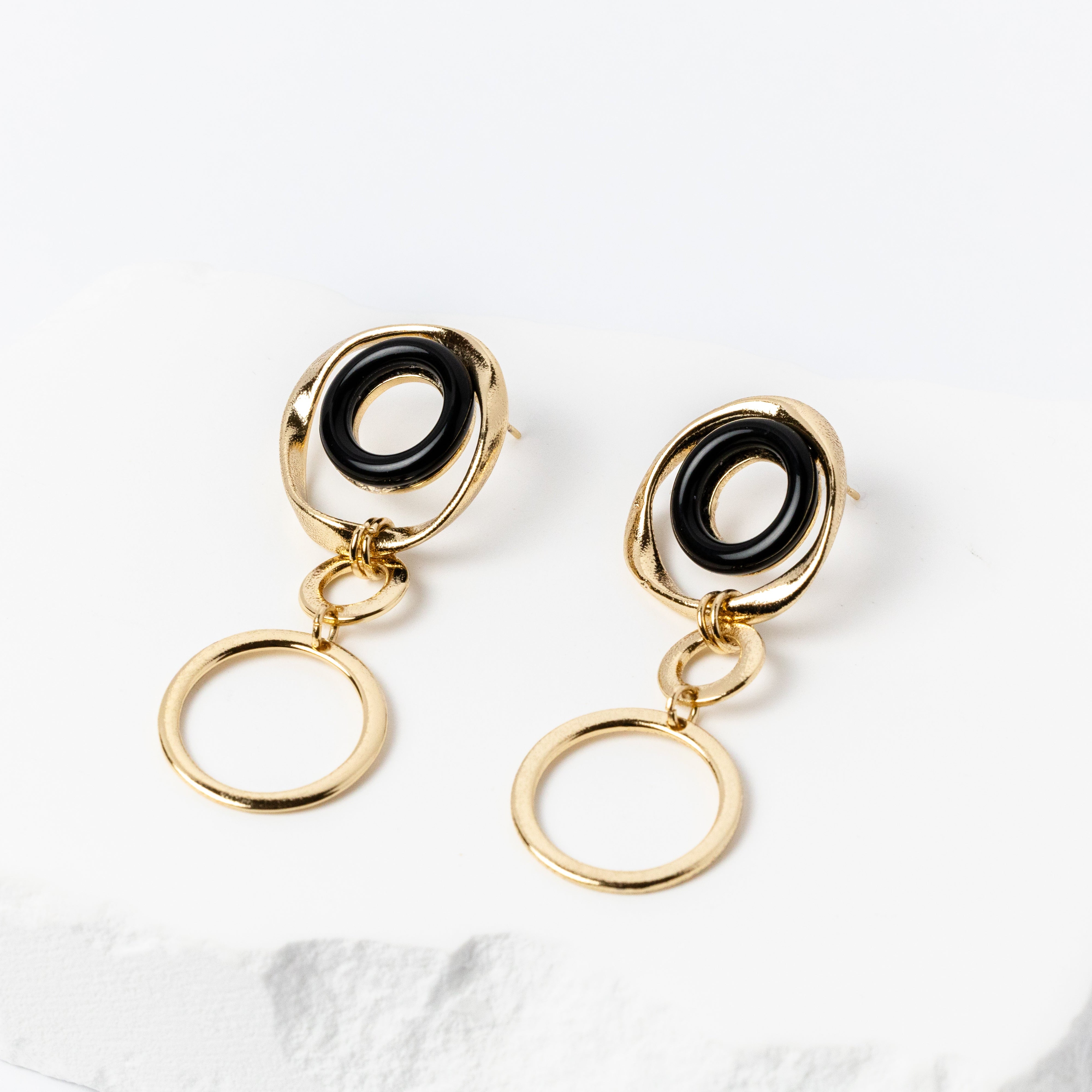 Handcrafted gold-plated drop earrings featuring polished donut-shaped black onyx gemstones framed by organic golden ovals, with interconnected open circles creating a sculptural, contemporary silhouette.