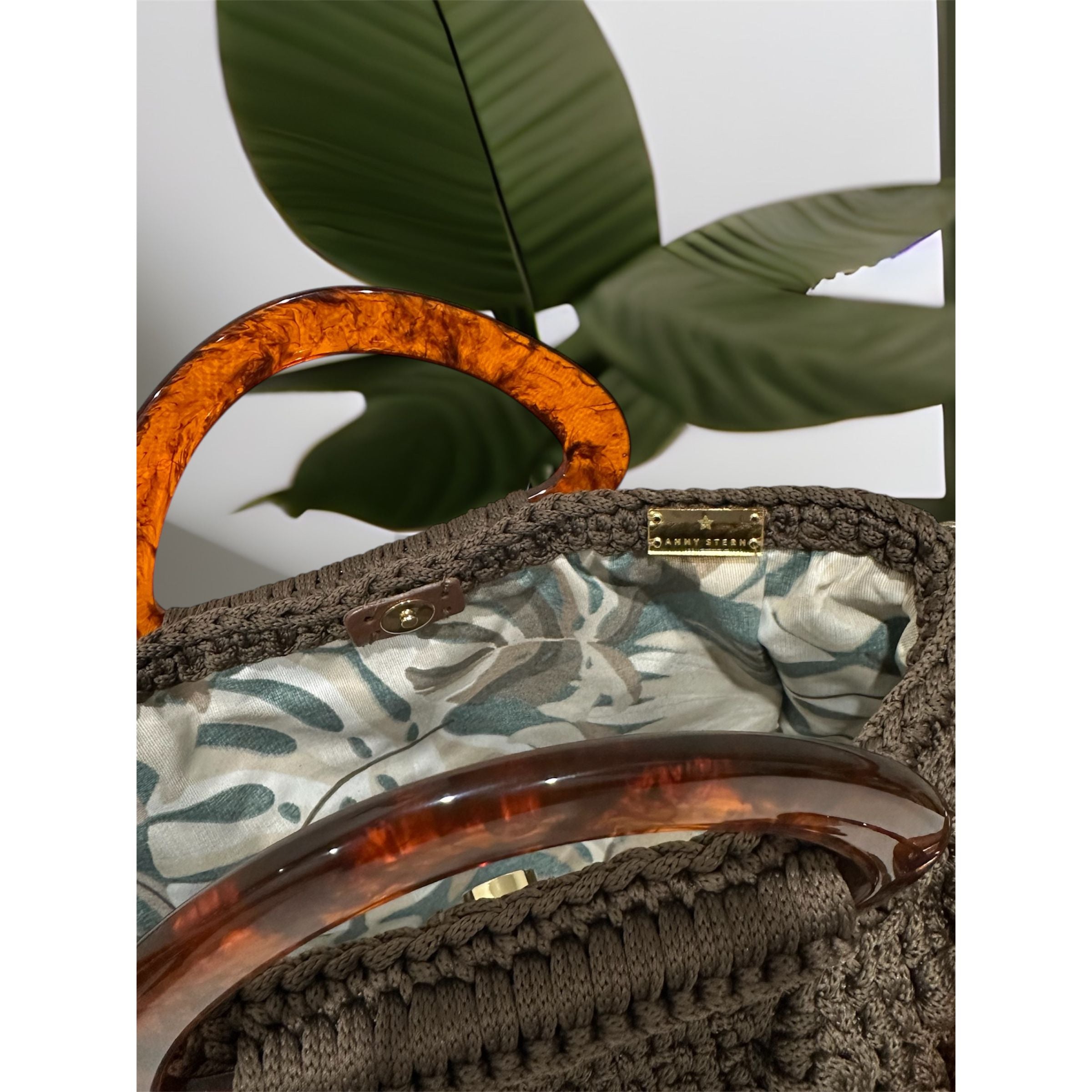 Interior view of the Paloma handbag · Wood & Water, featuring a bold botanical leaf lining in soft green and neutral tones, framed by the structured crochet body and finished with refined resin handle details.