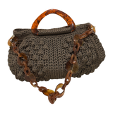 Hand-crocheted Paloma handbag in an earthy wood-toned hue with subtle green undertones and dimensional textured stitching, featuring a marbled amber resin top handle and a coordinating chain strap.