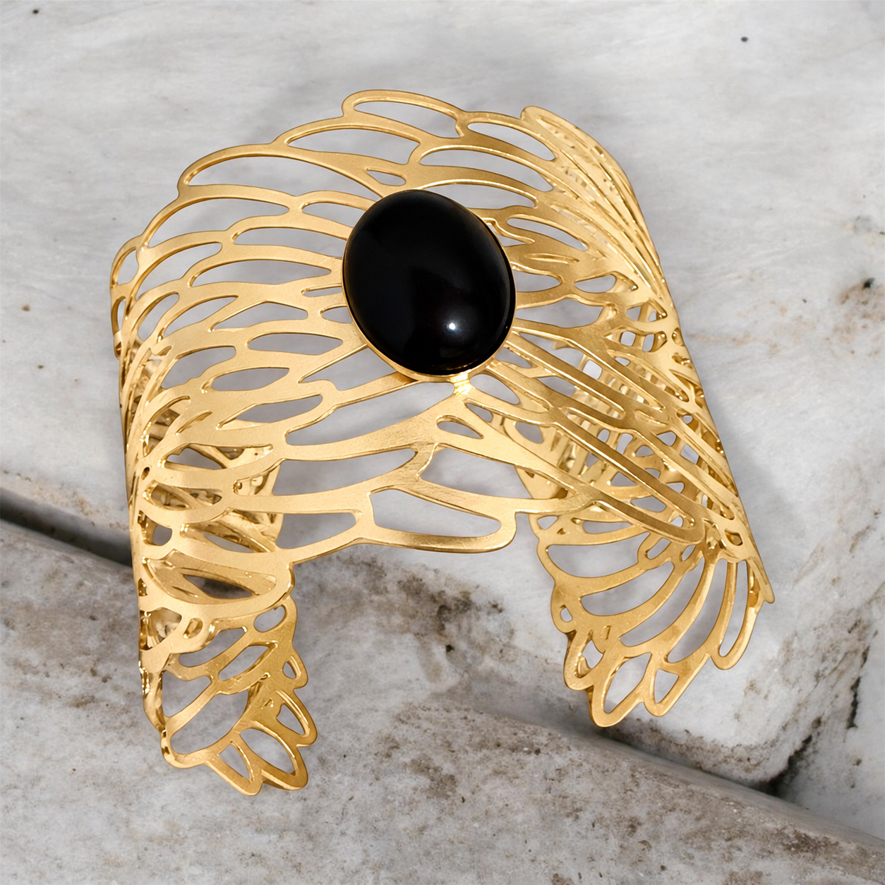 Angled view of the Golden Symphony Cuff highlighting its polished oval black onyx cabochon, sculptural golden openwork, and gracefully curved silhouette.