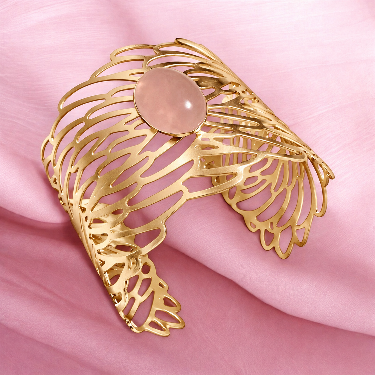Golden Symphony Cuff with a polished oval rose quartz cabochon in soft blush pink, surrounded by flowing, sculptural golden openwork in a wide statement silhouette.