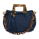 Hand-crocheted Giselle handbag in a deep midnight indigo tone with dimensional textured stitching, featuring marbled resin round handles, a coordinating chain strap, and tassel accents with polished bead details.