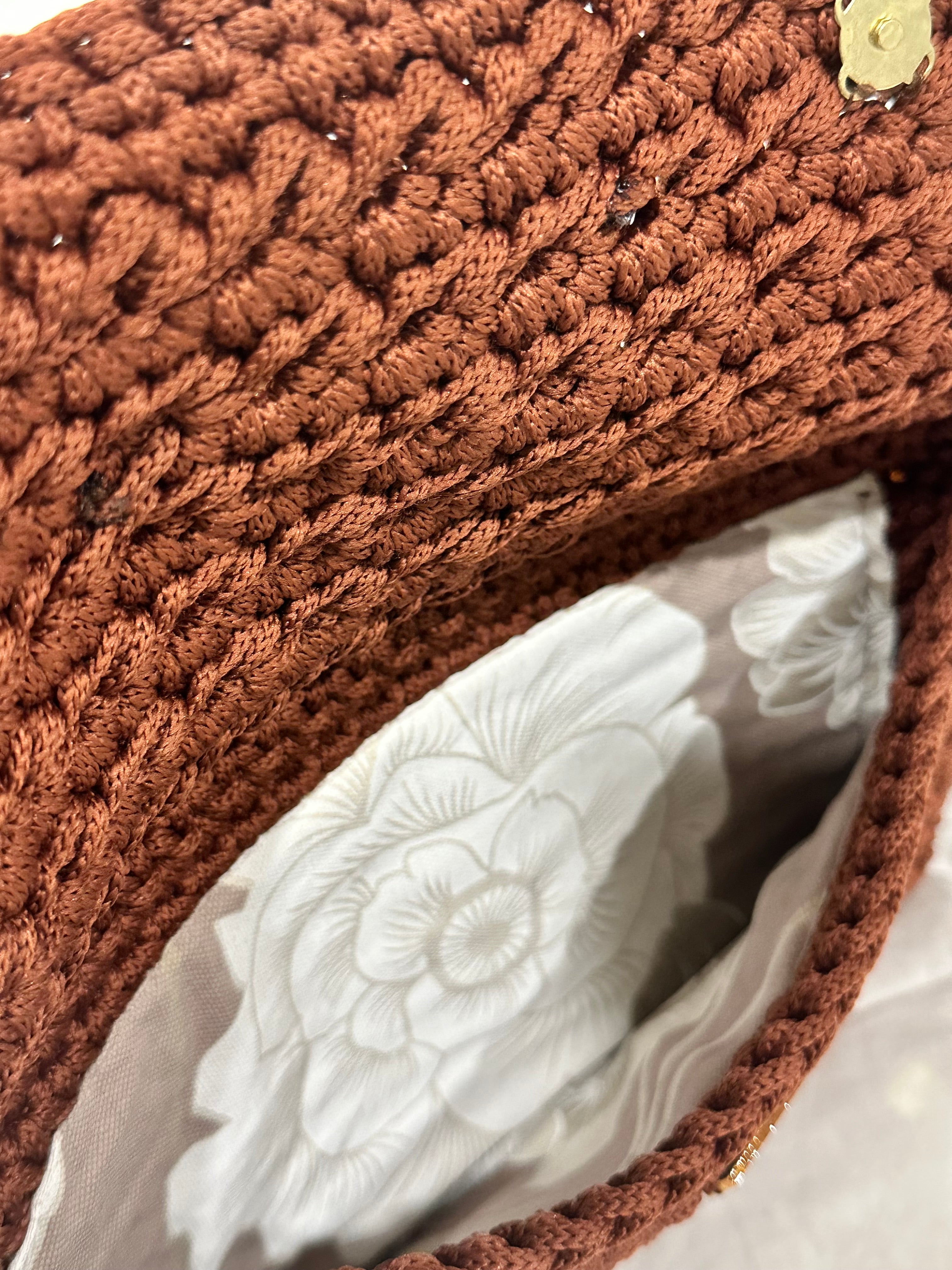 Interior view of the Polly Clutch showcasing textured cinnamon-brown crochet craftsmanship and a soft floral lining in layered ivory and warm neutral tones with secure magnetic closure detail.