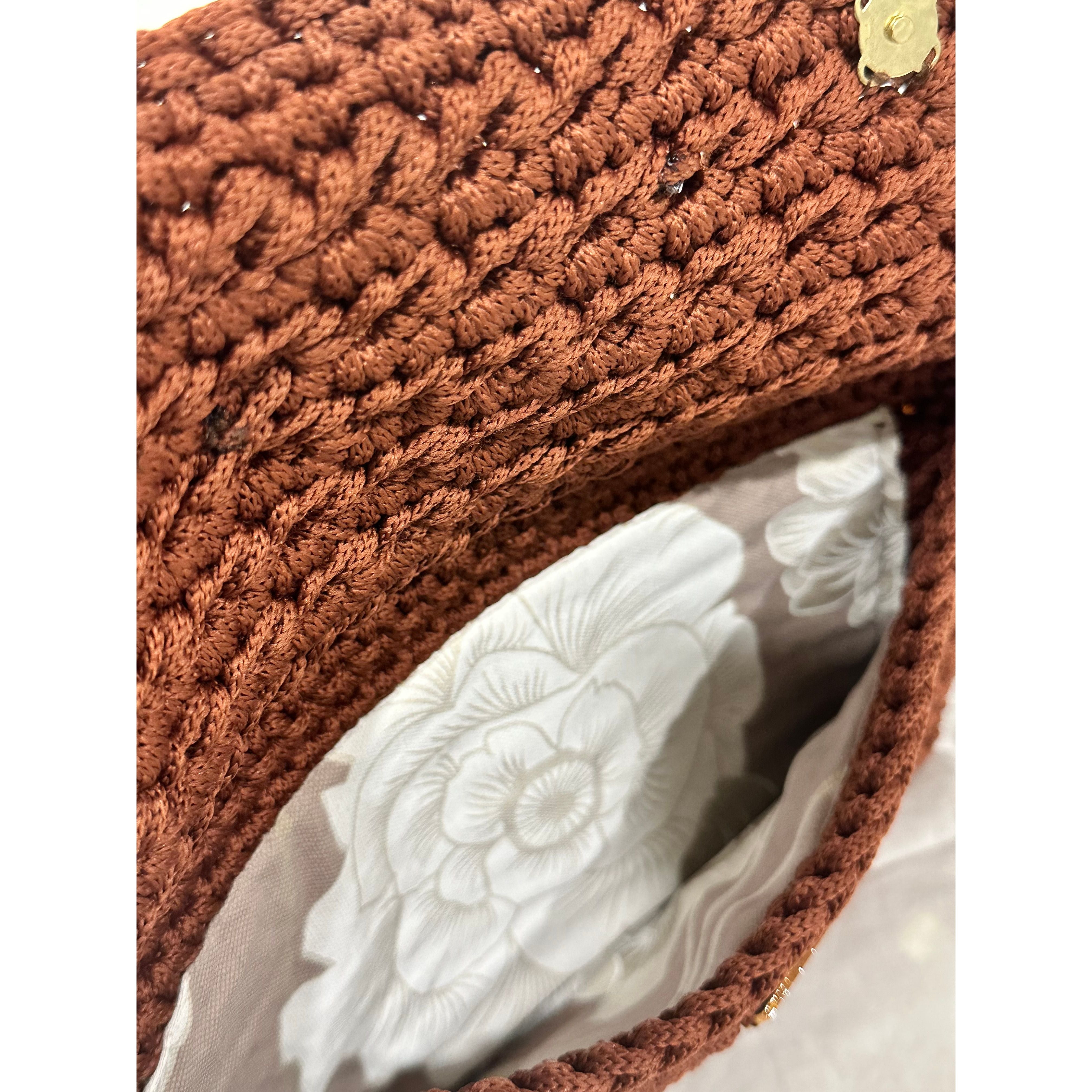 Interior view of the Polly Clutch showcasing textured cinnamon-brown crochet craftsmanship and a soft floral lining in layered ivory and warm neutral tones with secure magnetic closure detail.