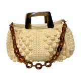 Hand-crocheted Paloma handbag in a soft pale yellow tone with richly textured stitching, featuring a sculptural marbled resin top handle and a coordinating resin chain strap.