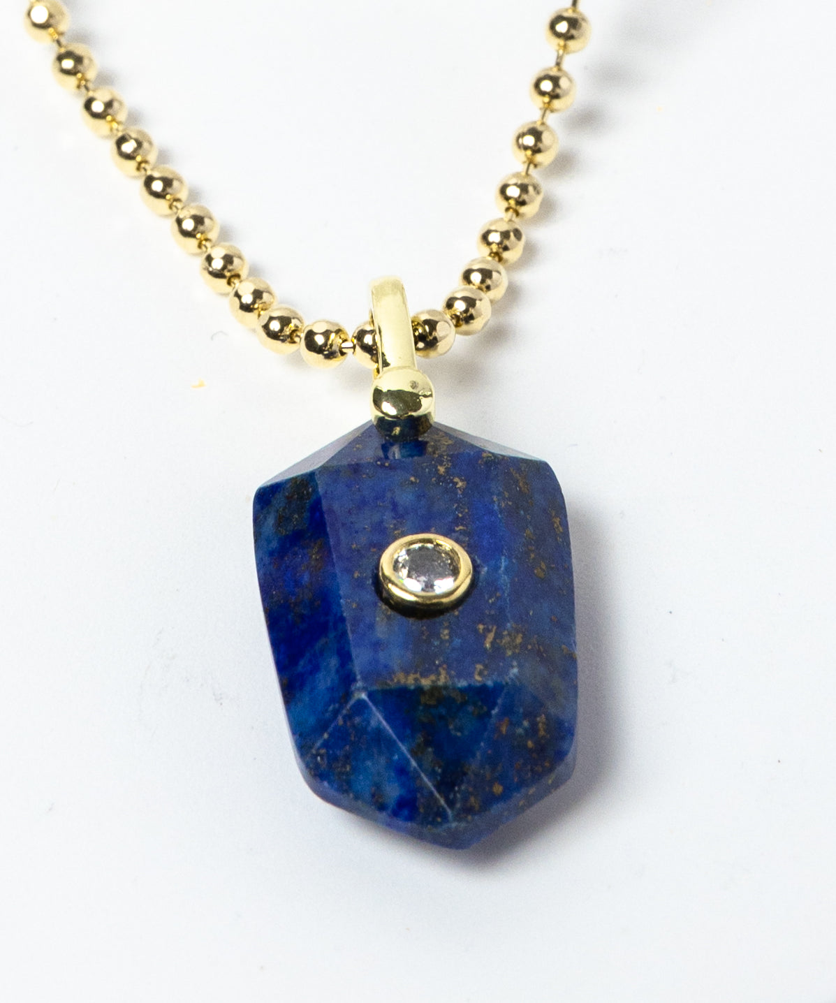 Close-up of a natural Lapis Lazuli pendant showcasing deep royal-blue tones, natural golden inclusions, faceted geometric shape, cubic zirconia detail, and gold-plated setting.