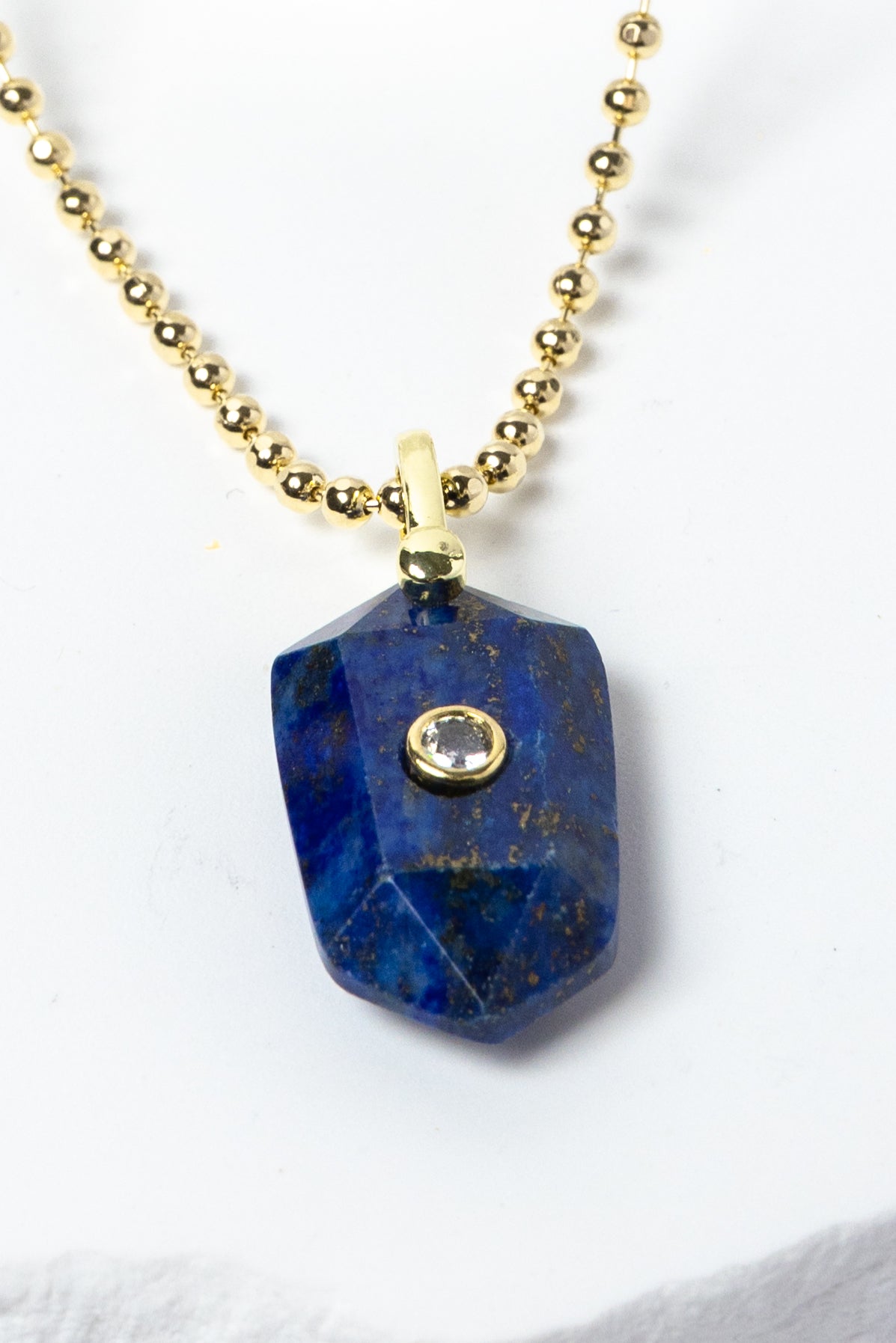 Close-up of a natural Lapis Lazuli pendant showcasing deep royal-blue tones, natural golden inclusions, faceted geometric shape, cubic zirconia detail, and gold-plated setting.