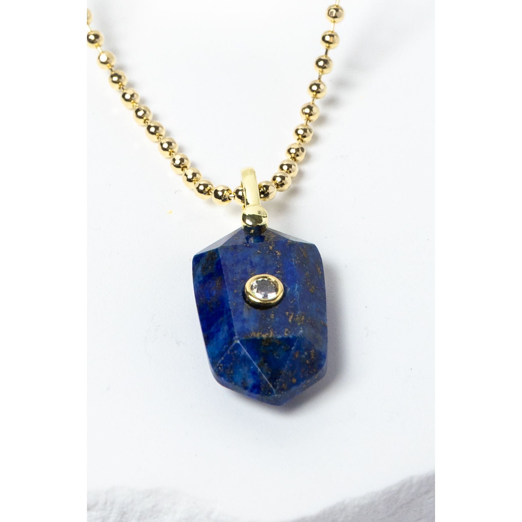 Close-up of a natural Lapis Lazuli pendant showcasing deep royal-blue tones, natural golden inclusions, faceted geometric shape, cubic zirconia detail, and gold-plated setting.