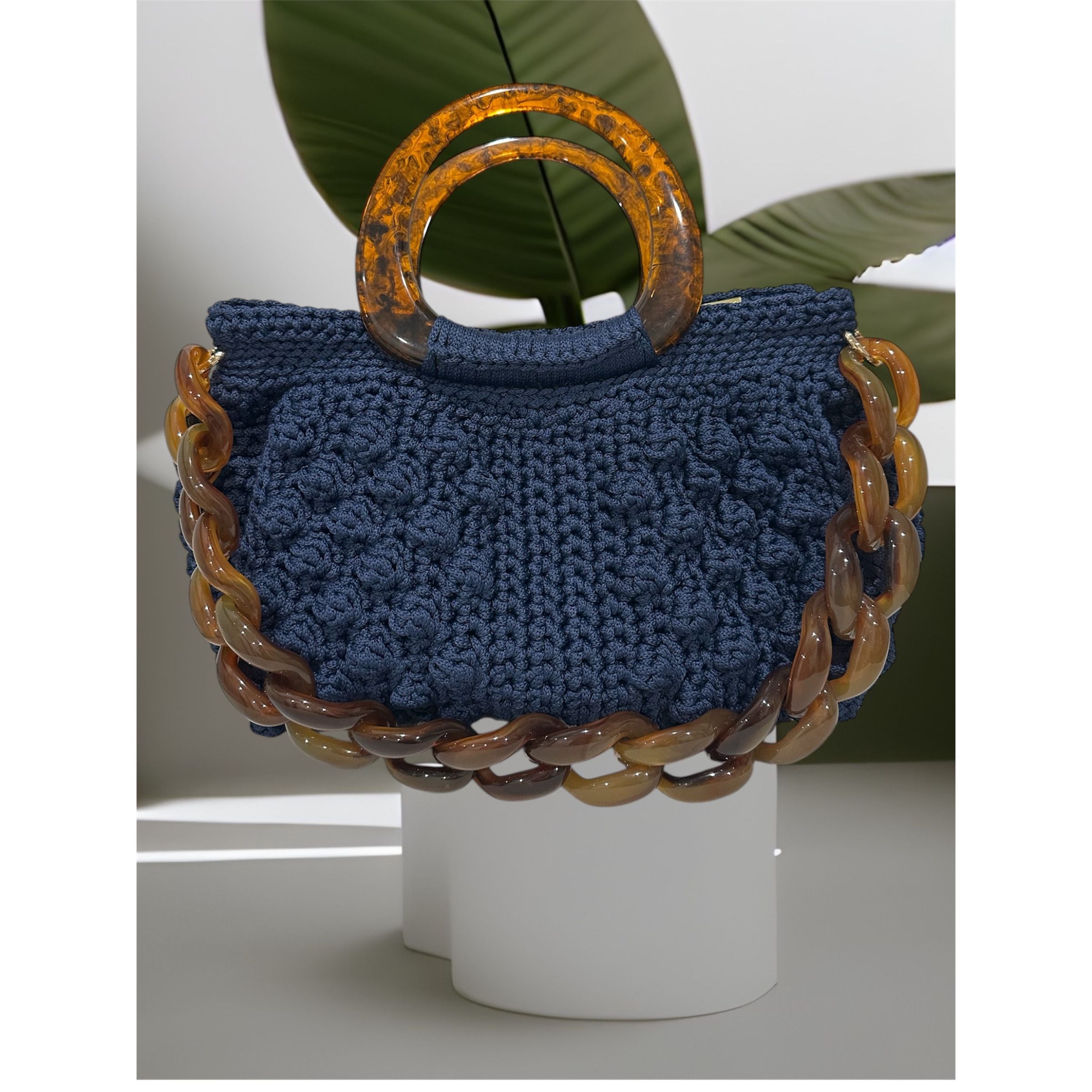 Hand-crocheted Paloma handbag in a deep sapphire blue tone with dimensional textured stitching, featuring a marbled resin top handle and a coordinating chain strap.