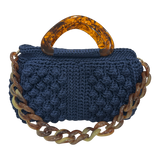 Hand-crocheted Paloma handbag in a deep indigo-blue tone with dimensional textured stitching, featuring a sculptural resin top handle and a coordinating chain strap.