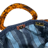 Interior view of the Paloma handbag · Deep Harbor, showing a striped fabric lining in tonal blue hues, framed by the structured crochet body and finished with refined resin handle details.