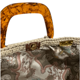 Interior view of the Giselle handbag, revealing an ornate patterned lining inspired by the Belle Époque era, framed by the softly structured crochet silhouette and finished with refined resin handle details.  